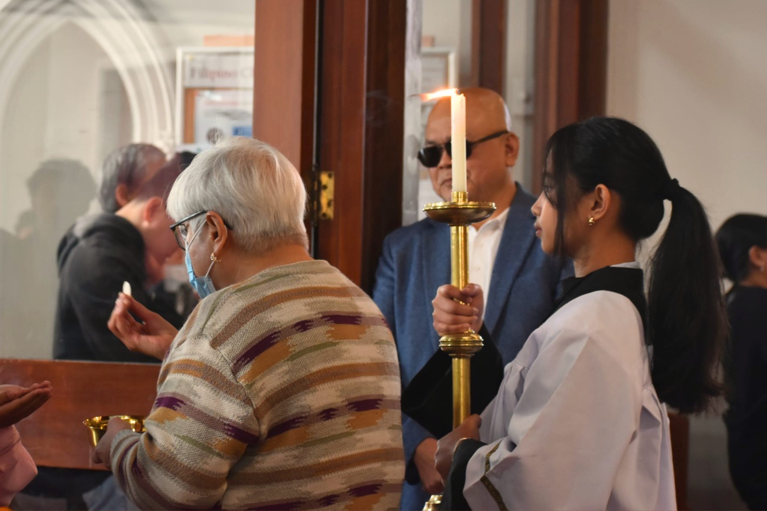 A minister giving Holy Communion to an elderly parishioner as an altar server holds a candle