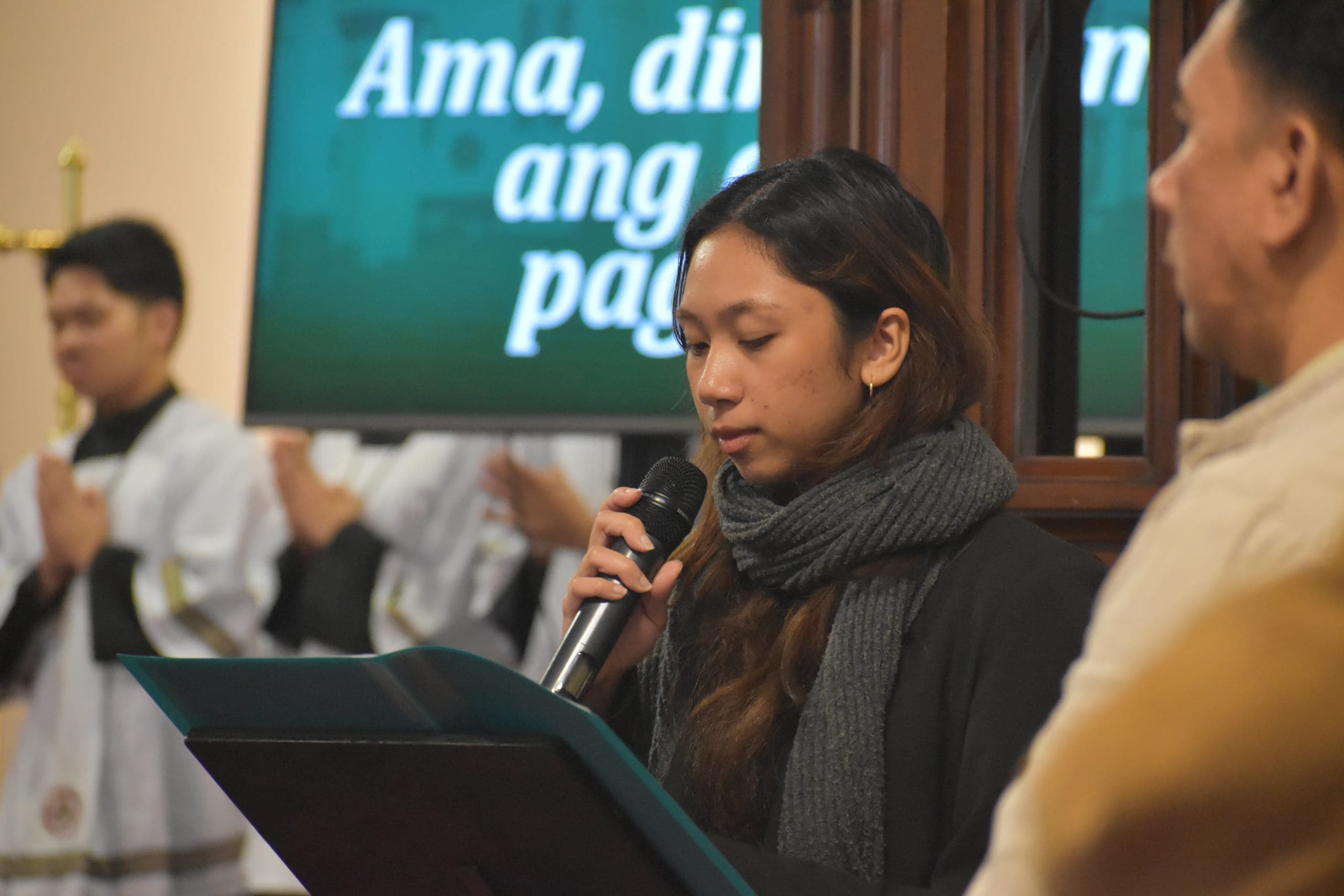 A lector reading into a microphone at the lectern during Mass