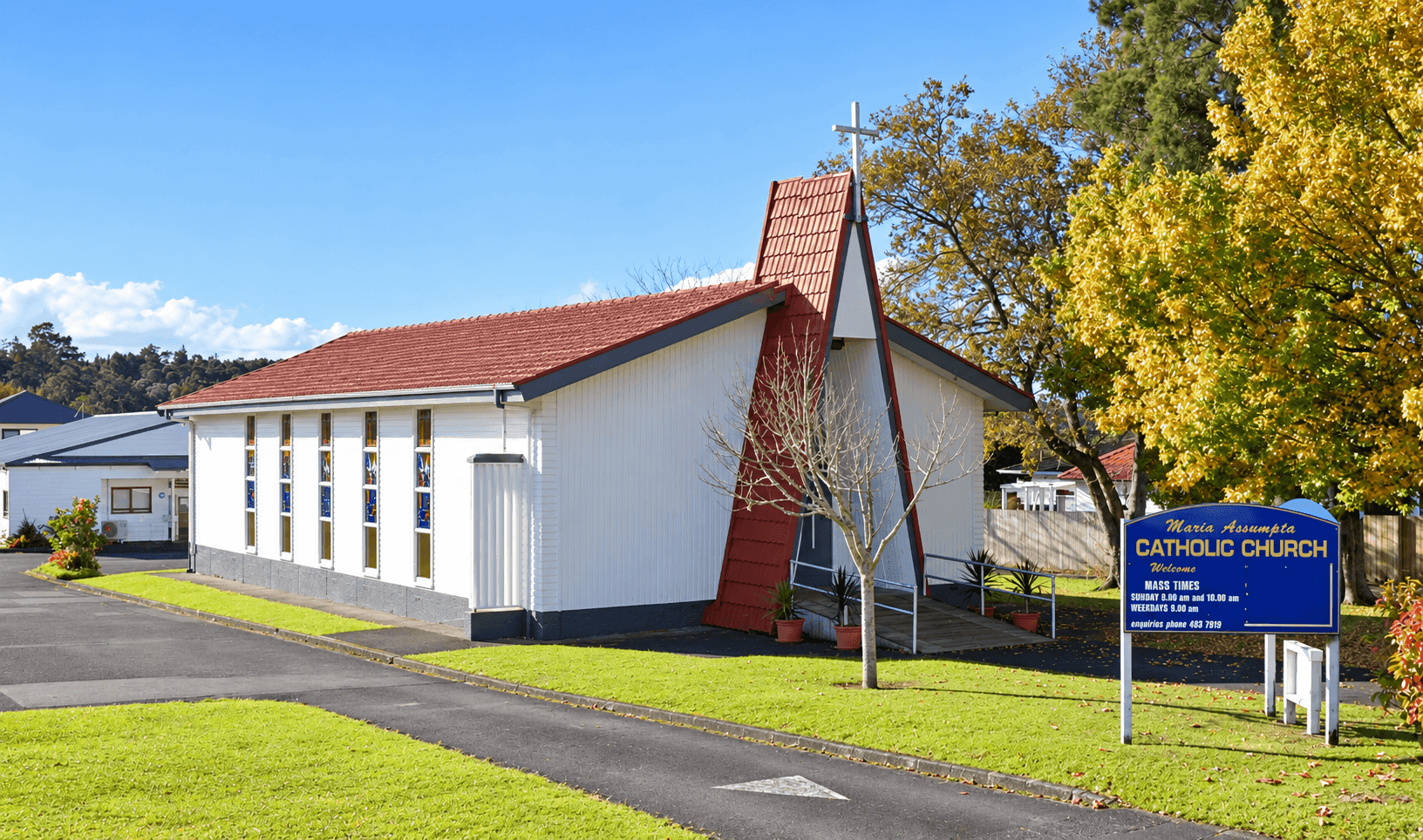 White Maria Assumpta Catholic Church with its red A-frame entrance and parish sign